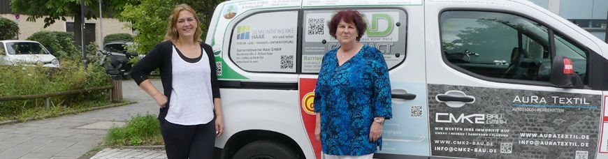Zwei Mitarbeiterinnen der Nachbarschaftshilfe Haar stehen vor dem neuen Fahrzeug, welches durch Werbung finanziert wurde.